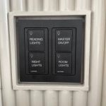 Stock photo showing the light switches in a luxury hotel in India. The light switches are black, with white, block capitalised text used to label their purposes. The wall these switches are situated on is a corrugated wooden wall, with glossy white paint.